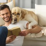 Millennial man reads to dog. Millennial increasingly choosing dogs over kids.