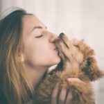 Woman kisses miniature poodle. The 2018 General Social Survey shows dog owners are twice as happy as cat owners.