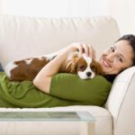 Woman snuggles on couch with Cavalier King Charles Spaniel.