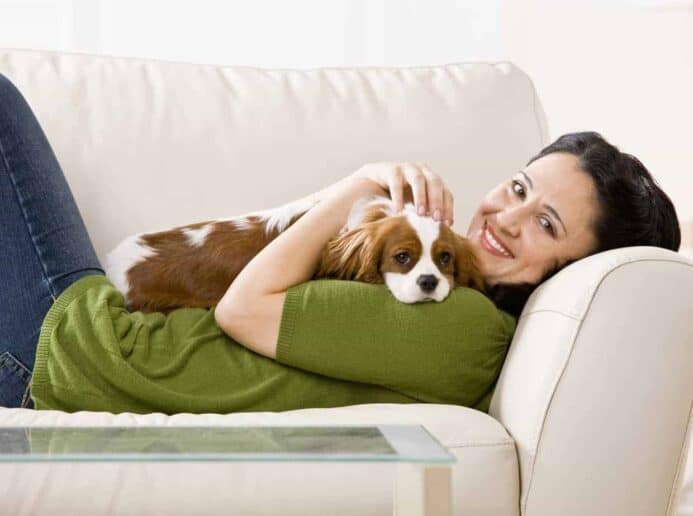 Woman snuggles on couch with Cavalier King Charles Spaniel.