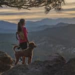 Woman hikes in Rocky Mountains with her poodle. Use exercise, grooming, training, treats, and affection to build a strong connection with your rescue dog and create long-lasting memories.