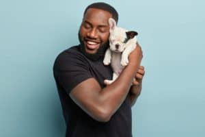 Man cuddles with a French bulldog puppy. Adopting a dog during quarantine has clear advantages, but consider your time, housing, and finances before making a decision.
