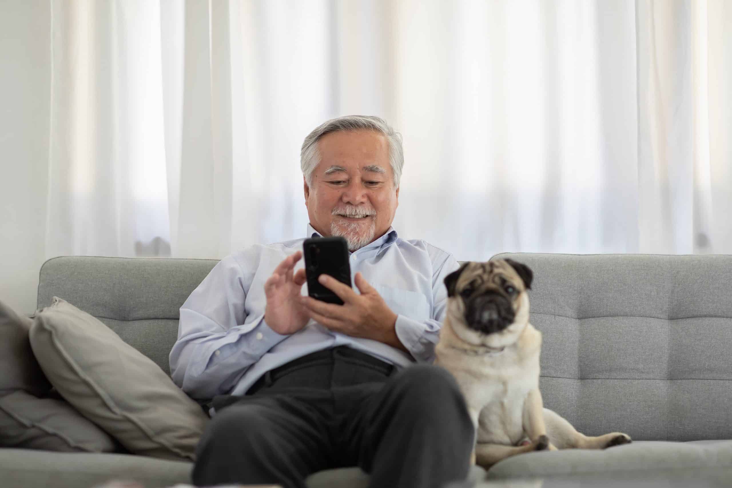 Older man sits on couch with pug. Bellewood, a retirement and assisted living residence in Kirkland, WA, offers pet-friendly apartments and services like dog walking.