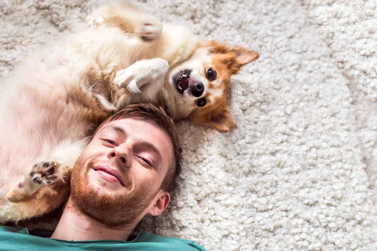 Man cuddles with puppy while lying on the floor. As a first-time dog parent, it’s your responsibility to look out for your dog's nutrition, health, and entertainment.
