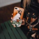 Woman poses with her miniature pinscher and her custom pet phone case.