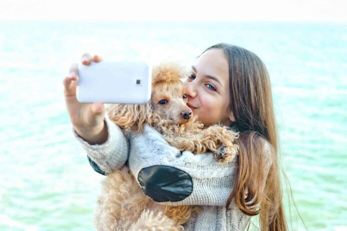 Owner takes selfie while holding her poodle. Creating a special social media account for your doggie is a way to share photos and videos of your pet without irritating your friends and family.