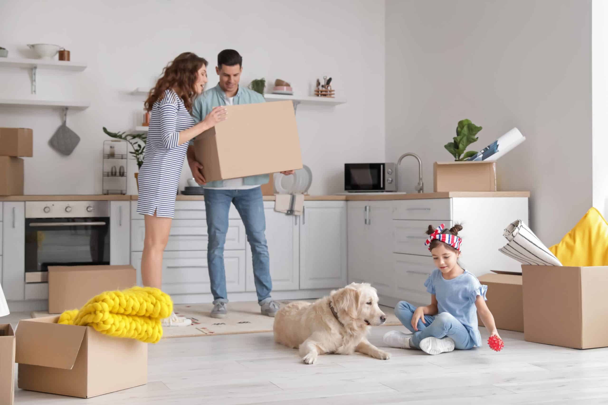 Girl plays with dog while her parents unpack the kitchen after moving. Plan ahead, take your time, and give your dog extra love and attention, to make moving with your dog as easy as possible for both of you.