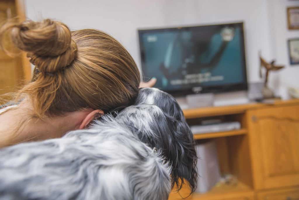 Woman points at TV while watching with dog. Photo for dog sounds post.