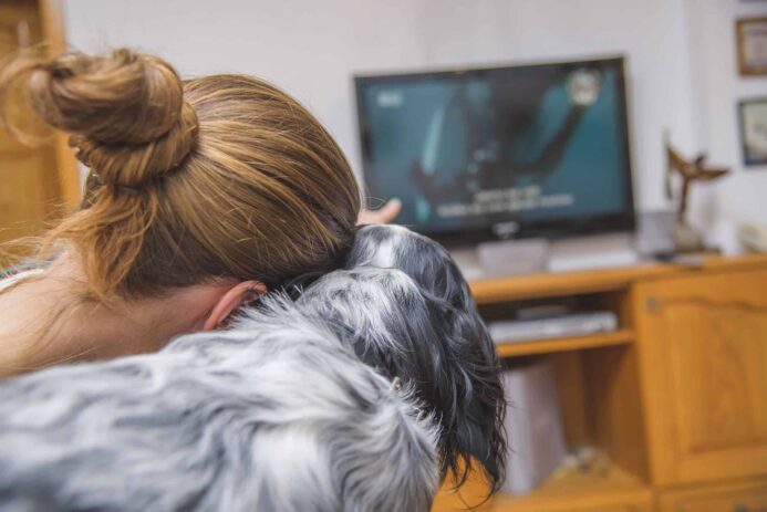 Woman points at TV while watching with dog. Photo for dog sounds post.