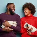 Loving couple gazes at each other while holding French Bulldog puppies. The best how we met stories include dogs that bring together dog lovers for their own happily ever after.