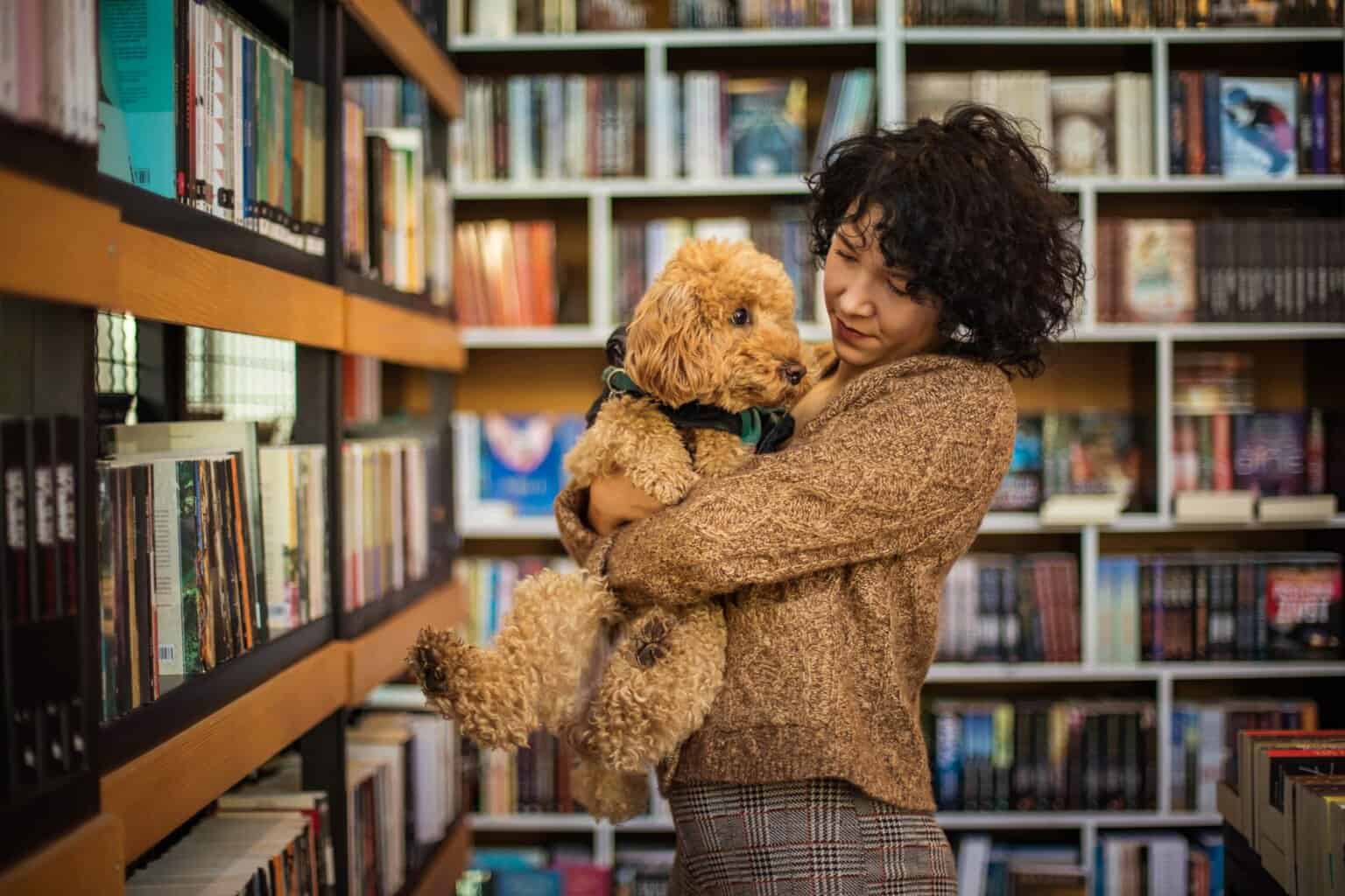 Female college student cuddles small labradoodle in library. Dogs provide mental health support and boost the well-being of college students. Dogs help reduce stress and make it easier to meet people.