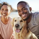 Couple poses on the beach with a Golden Retriever. No matter the living situation, single person or a couple, dogs need a loving and supportive home that provides care and consistency.