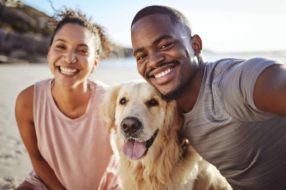 Couple poses on the beach with a Golden Retriever. No matter the living situation, single person or a couple, dogs need a loving and supportive home that provides care and consistency.