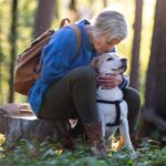 Older woman hikes with older dog. Use stimulating outdoor activities to promote both physical and mental wellness for aging dogs and their owners.
